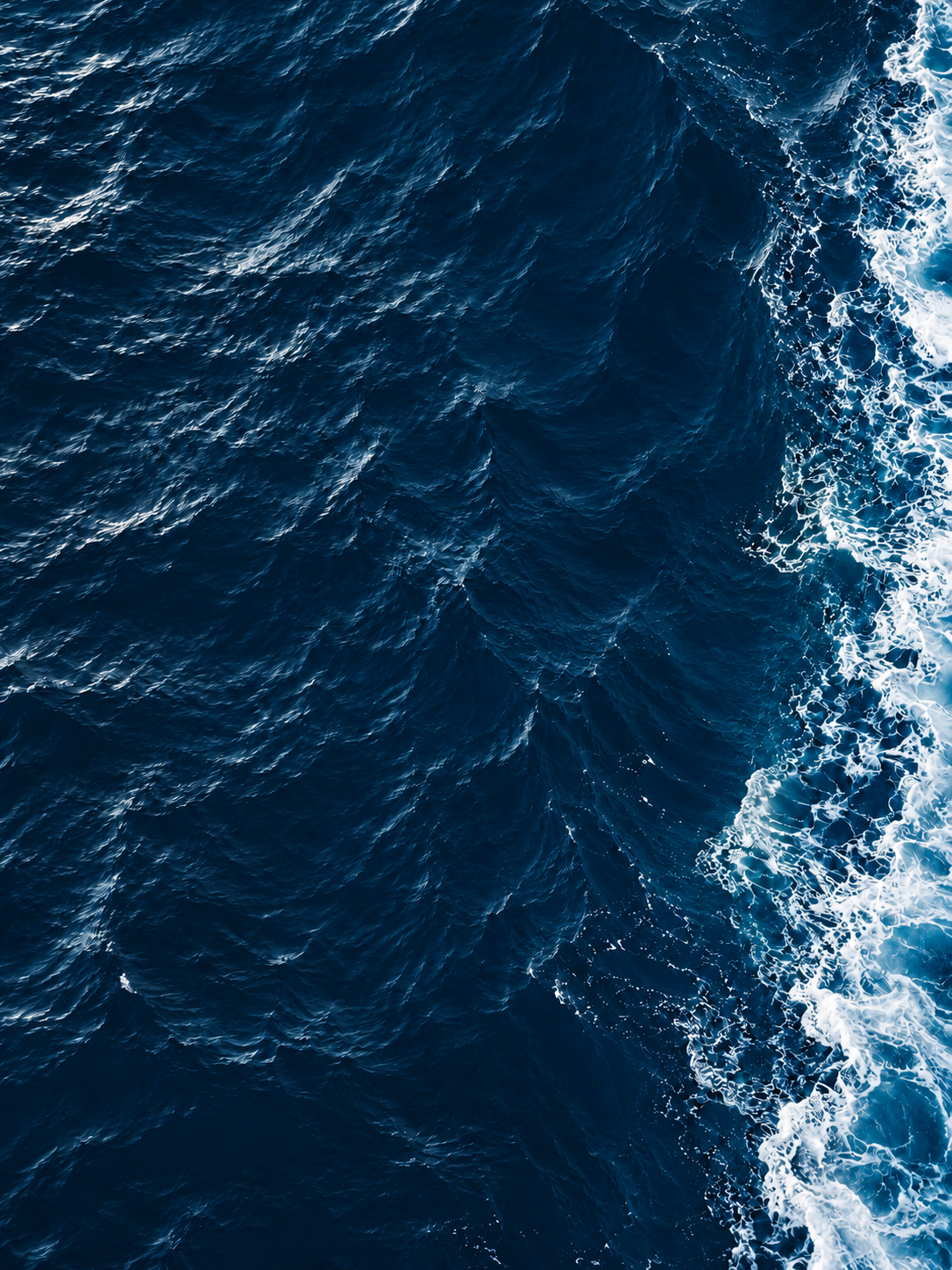 Deep blue ocean and white foam seen from above
